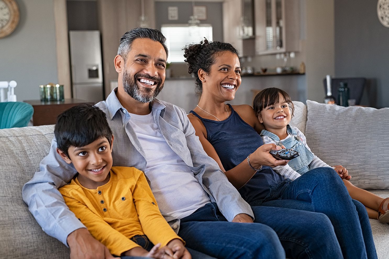 A family is sitting on a couch watching tv together.