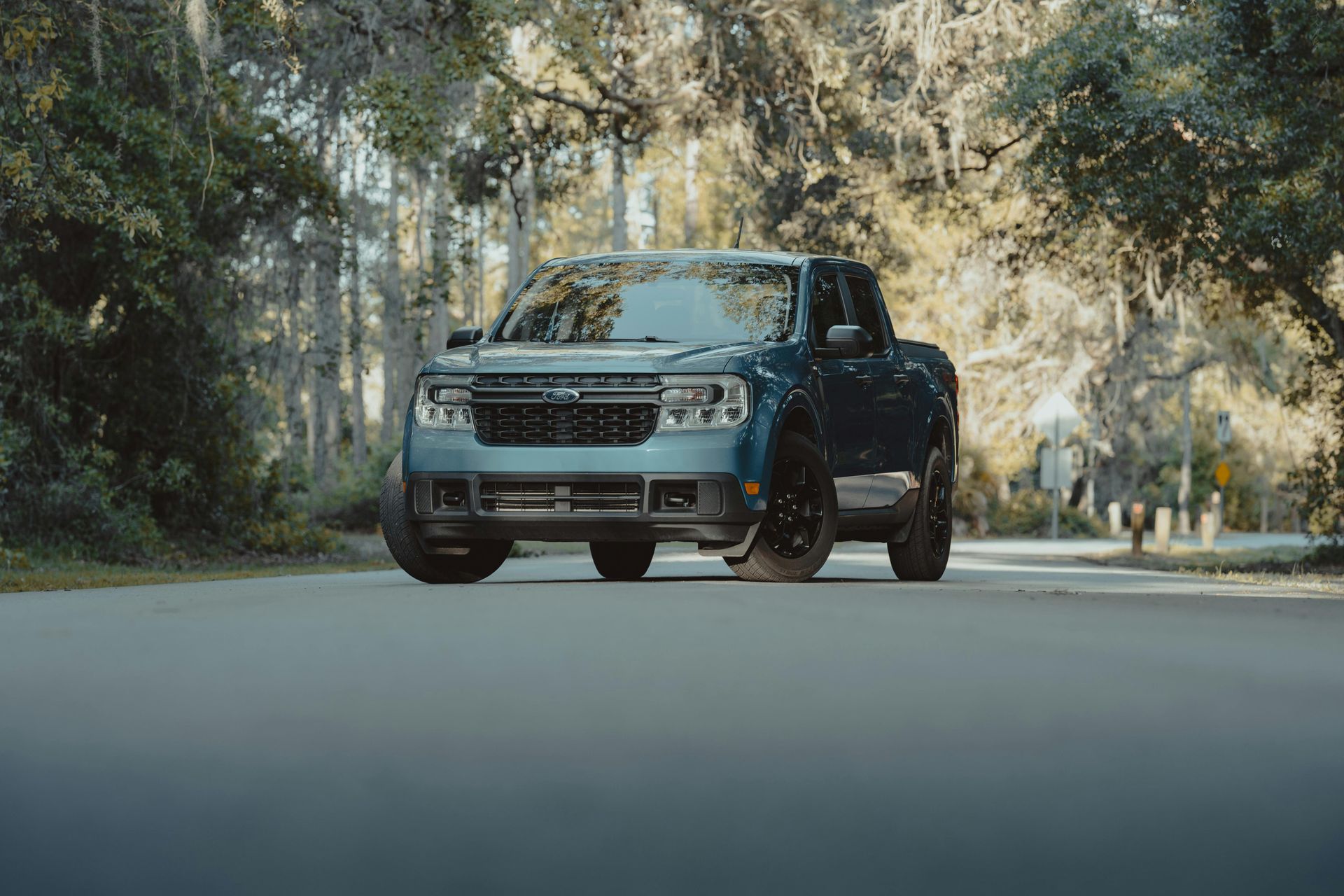A blue truck is driving down a road surrounded by trees.