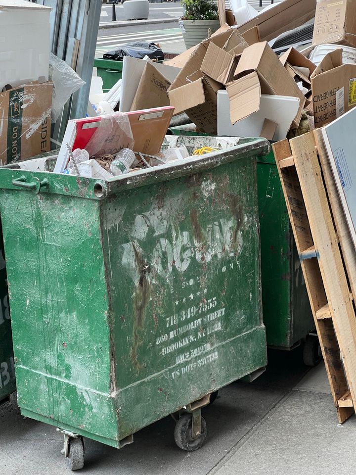 Overflowing green dumpster with cardboard boxes and trash on a street corner