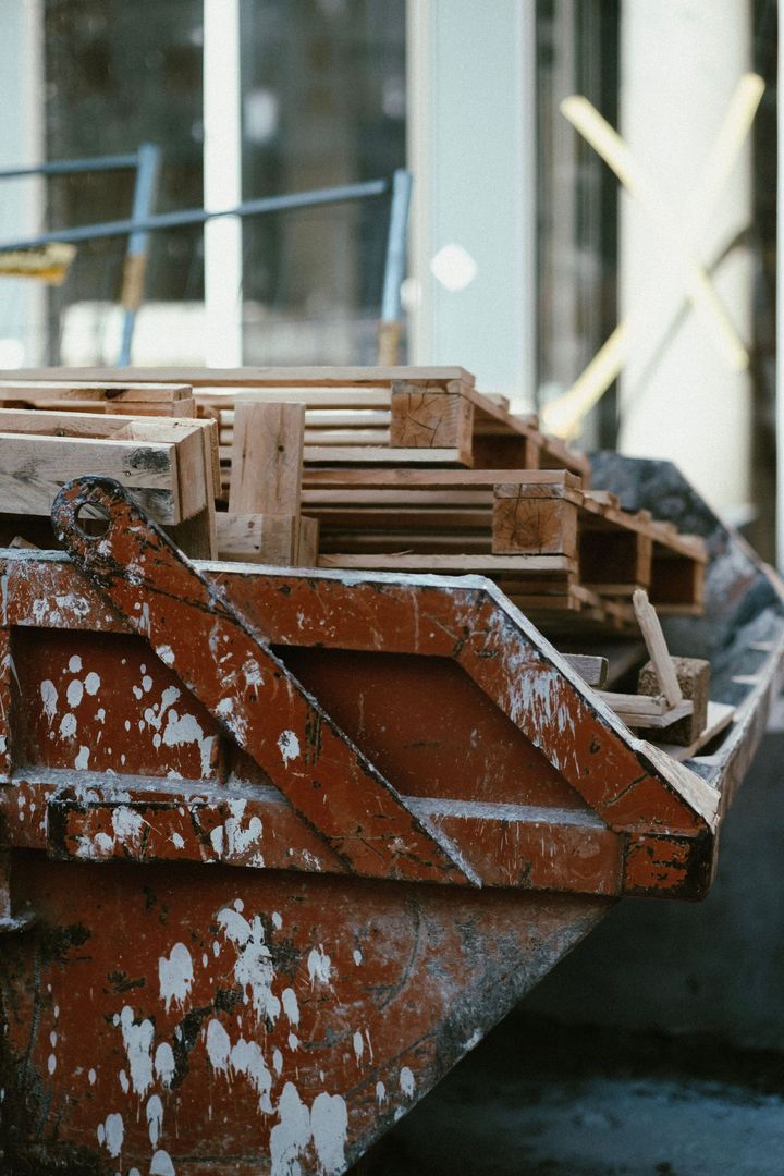 Rusty metal dumpster filled with stacked wooden pallets in an industrial area