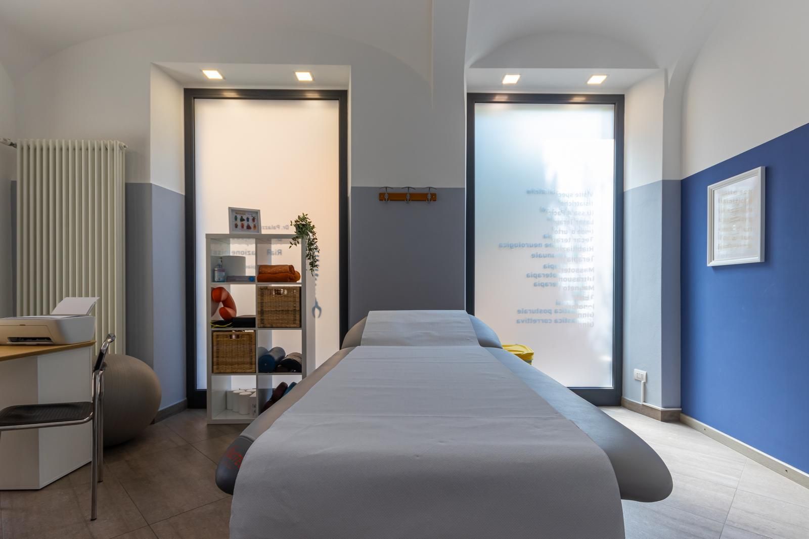 Sala massaggi con lettino per trattamenti, parete con dettagli blu, mensole e porte in vetro satinato.