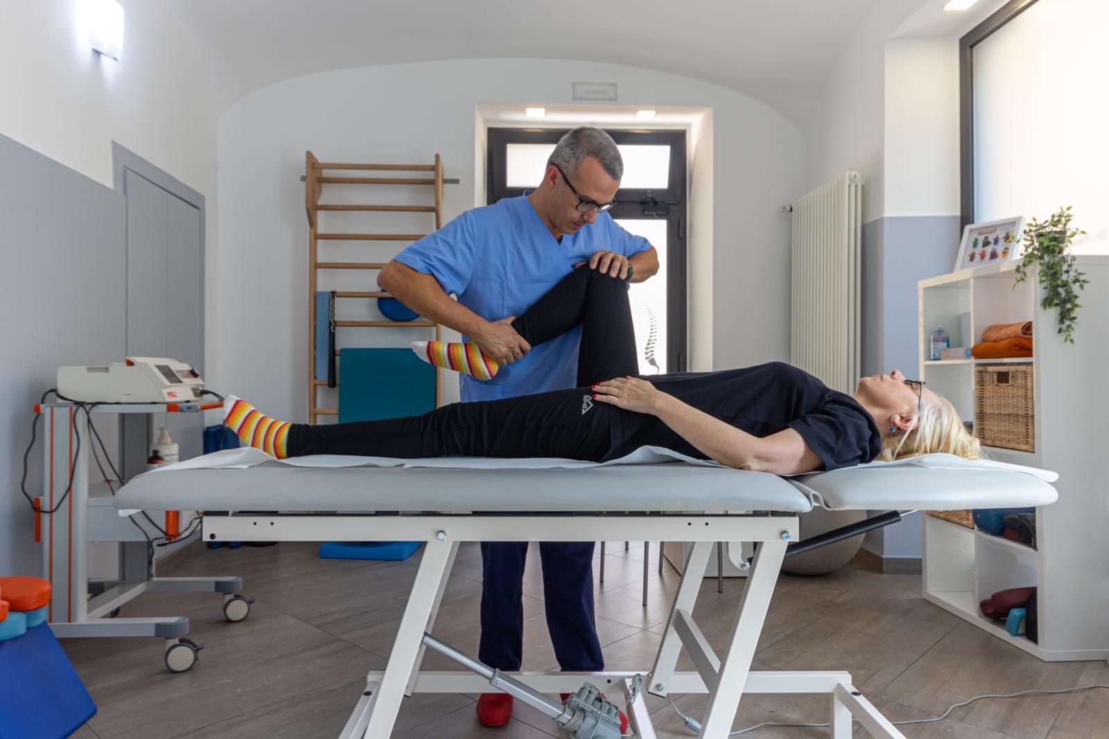 Fisioterapista assiste un paziente sul lettino da trattamento in una luminosa stanza della clinica.
