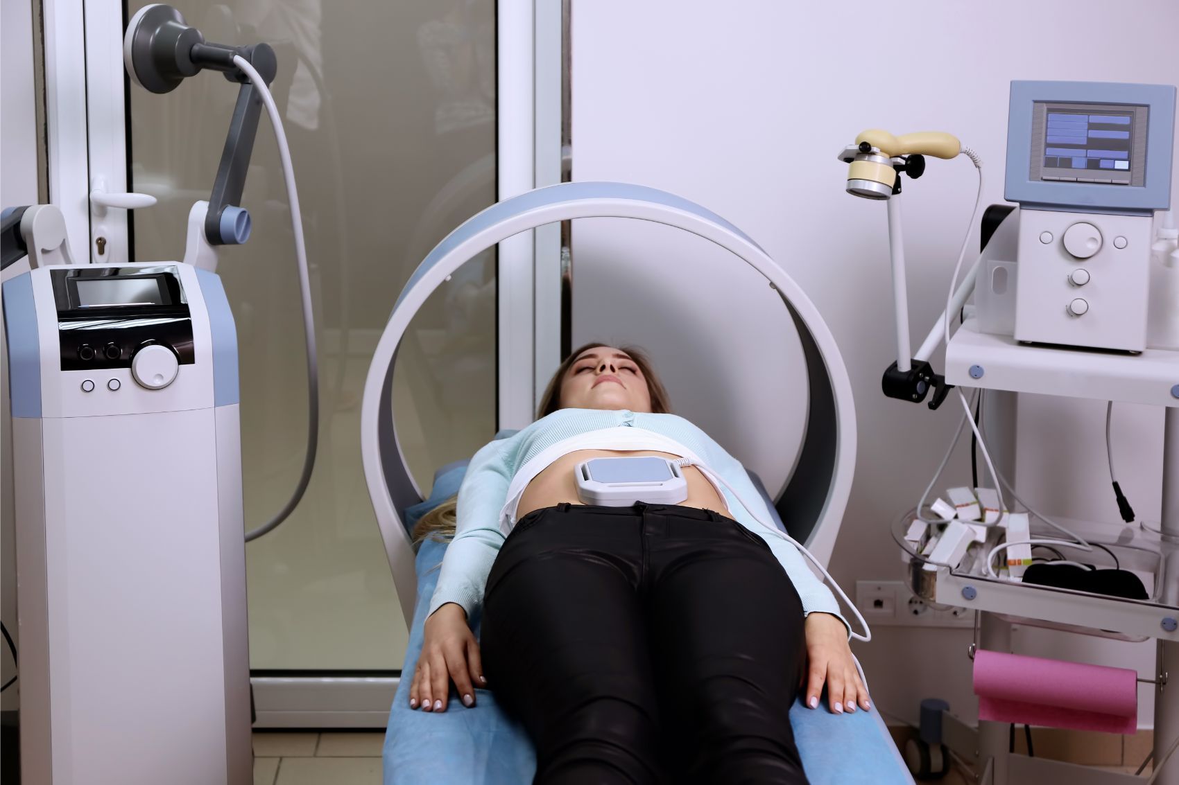Il paziente è sdraiato su un lettino per esami diagnostici, circondato da apparecchiature di imaging, in una stanza di una clinica.