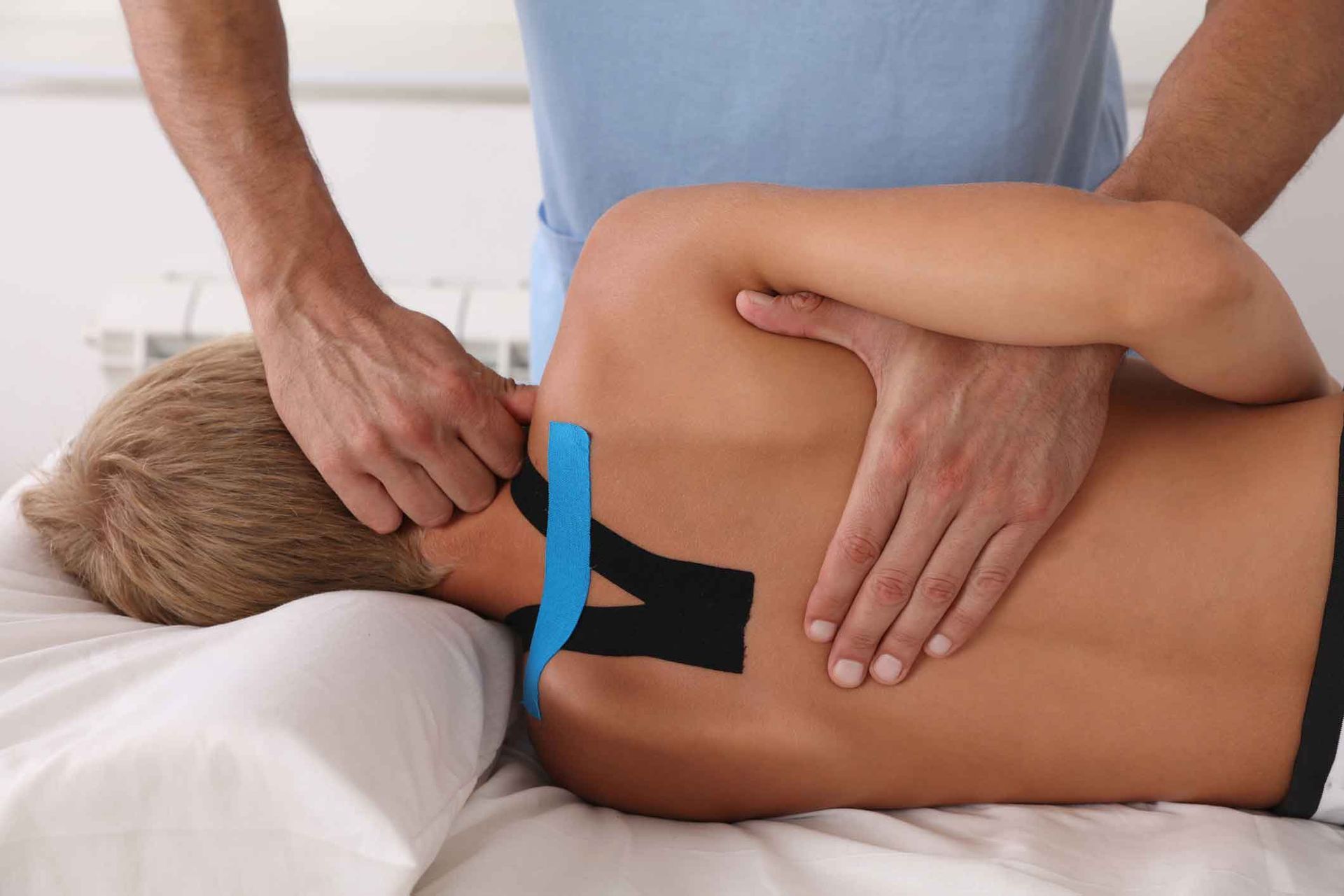 A woman is getting a massage from a man with kinesio tape on her back.