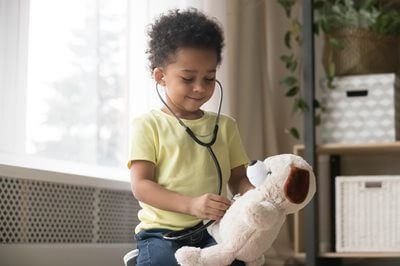 Child playing doctor with a stuffed dog in a bright room, using a stethoscope.
