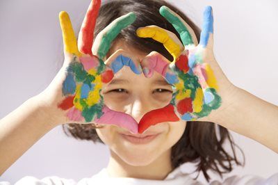 Child smiling with paint-covered hands framing their face in colorful handprints