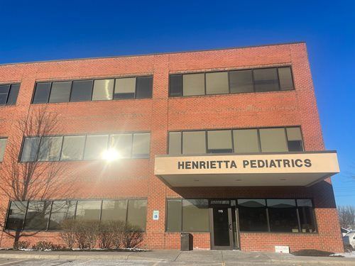 Brick pediatric clinic building with sign reading “Henrietta Pediatrics” under a clear blue sky