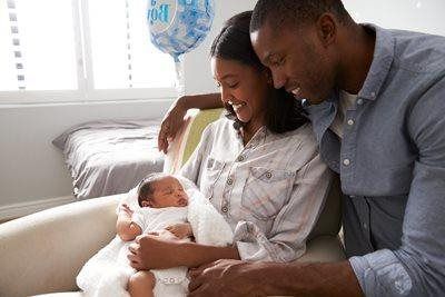 Parents smiling at a newborn baby on a couch in a bright living room