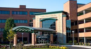 Modern hospital entrance with glass canopy, brick facade, and landscaped front drive