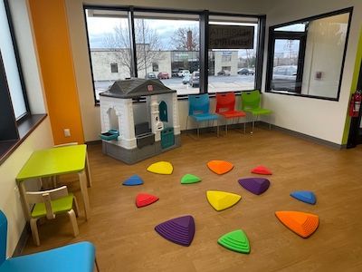 Bright playroom with colorful floor cushions, small tables, and a toy house by large windows