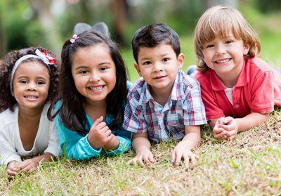 Four children lying on grass, smiling at the camera outdoors.