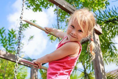 Smiling child climbing a wooden play structure outdoors on a sunny day