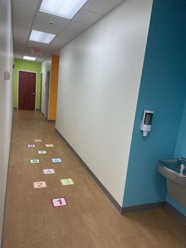 Hallway with numbered floor markers, white walls, blue alcove, and a water fountain on the right.