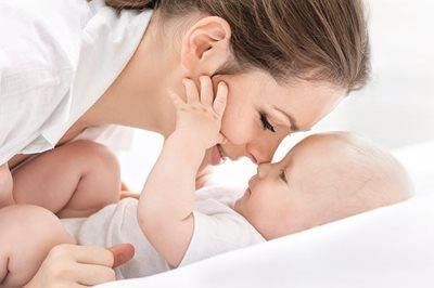 Parent kissing a baby lying on a white bed, both in white clothing