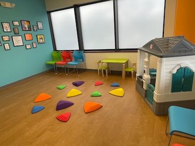 Bright playroom with colorful floor cushions, small chairs, wall art, and a toy house by the window.