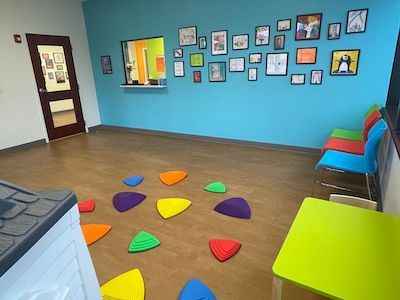 Colorful kids' playroom with floor cushions, chairs, framed wall art, and a small table