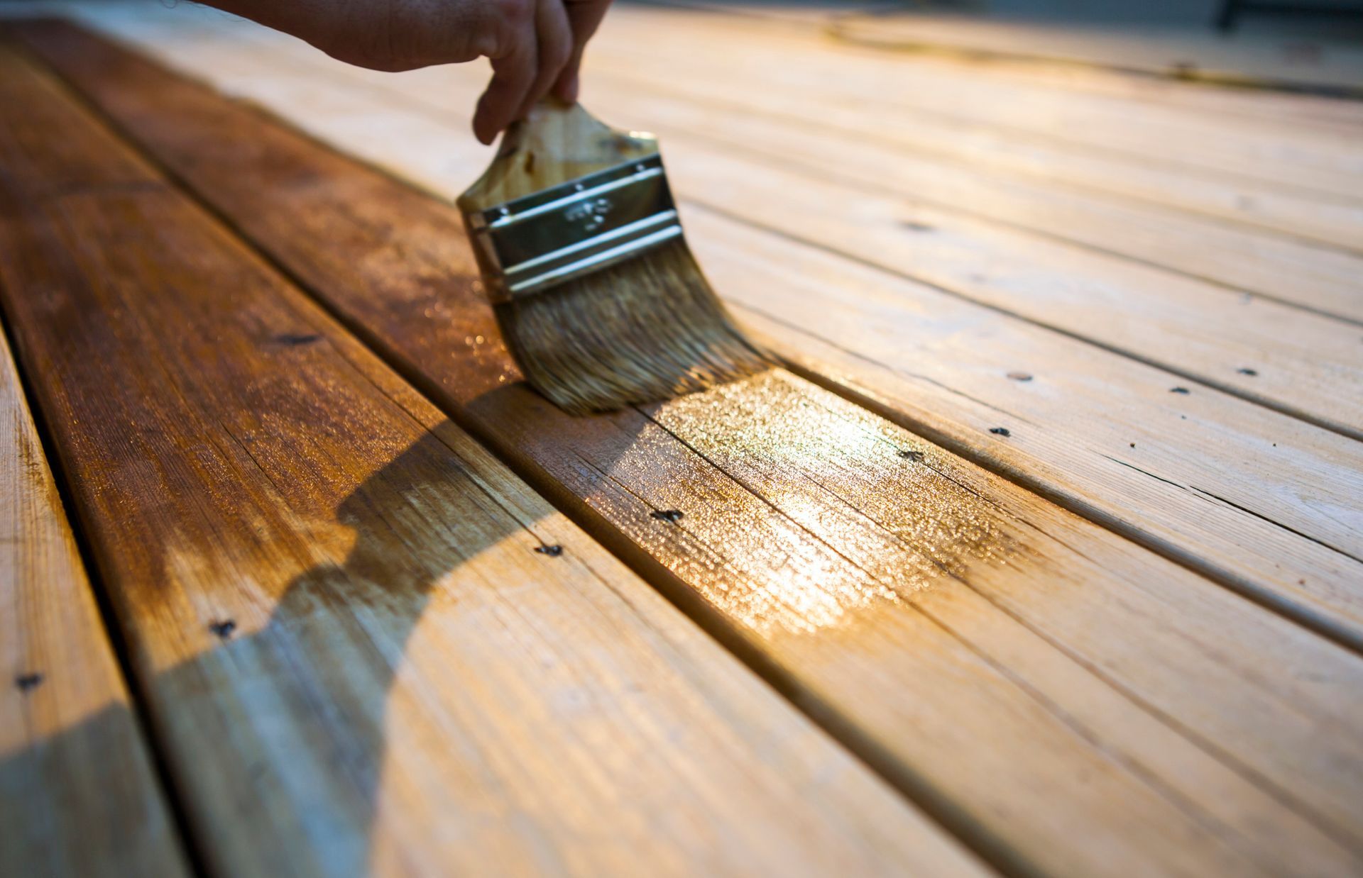 A person is varnishing a wooden deck with a brush.