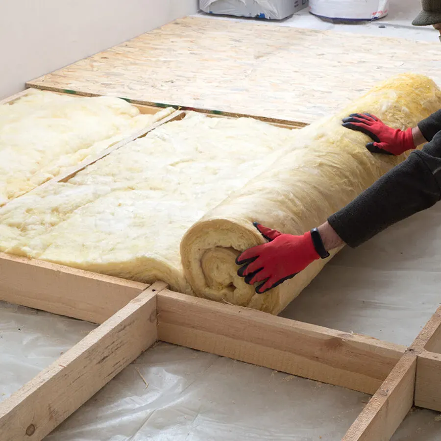 A person is rolling a roll of insulation on a wooden floor.