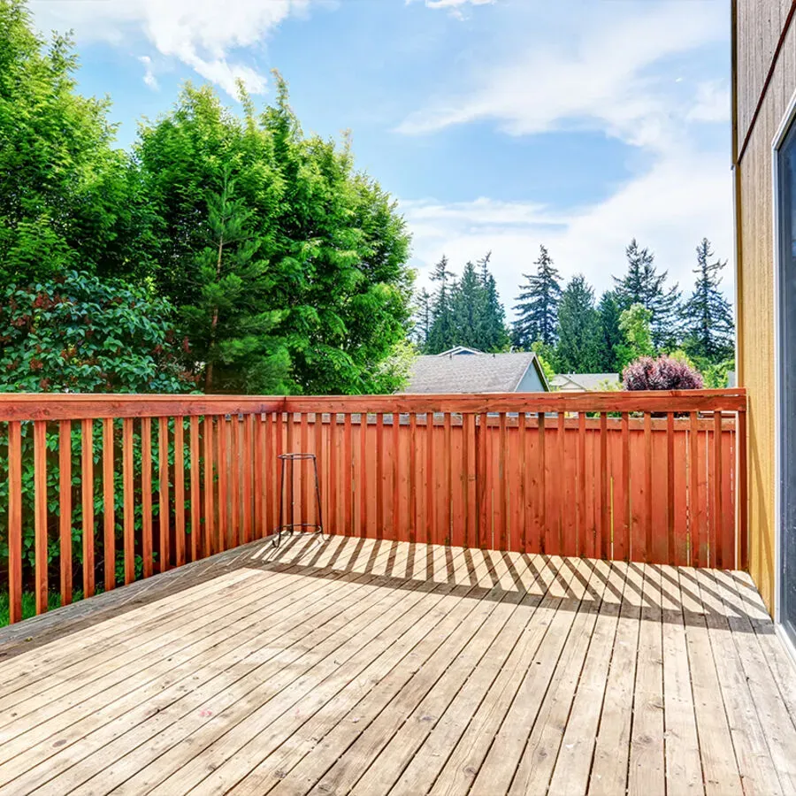 An empty wooden deck with a wooden fence and trees in the background.