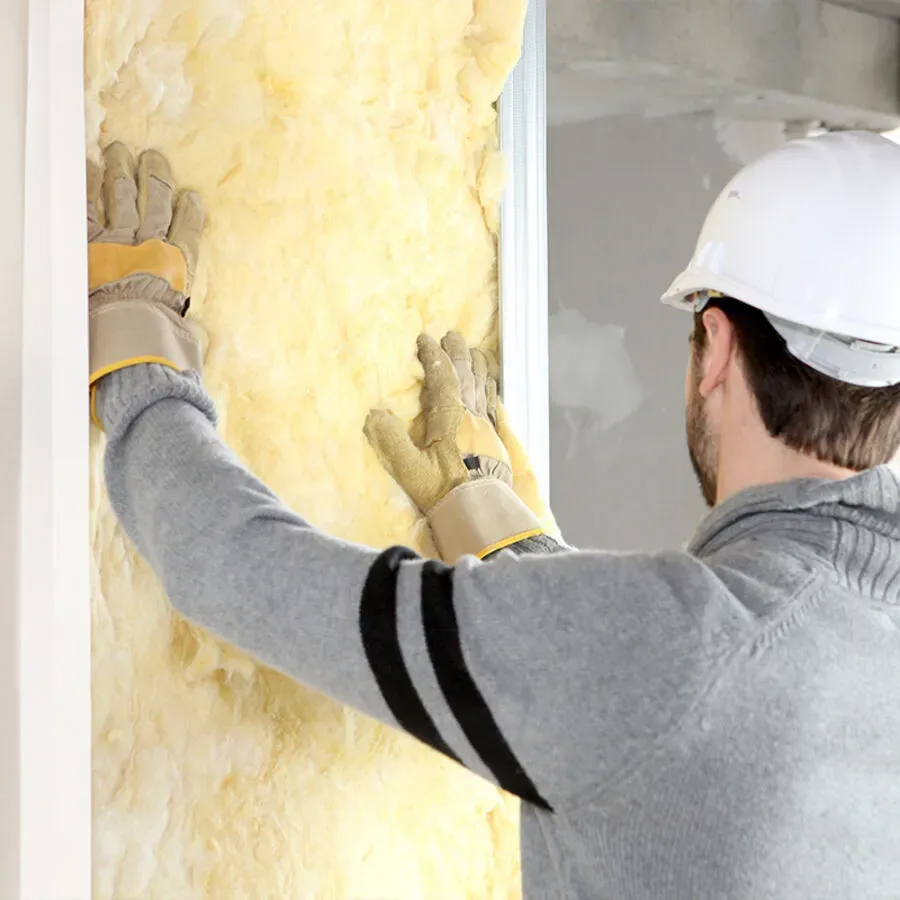 A man wearing a hard hat and gloves is insulating a wall