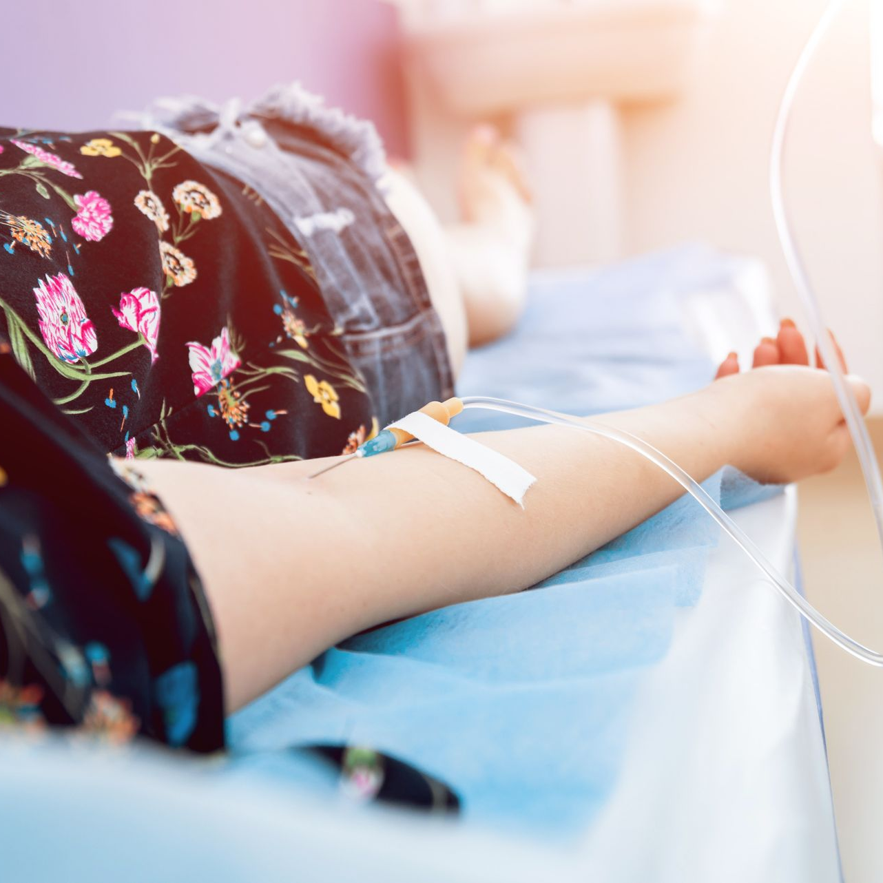 Person receiving IV fluids in a medical setting, arm extended.