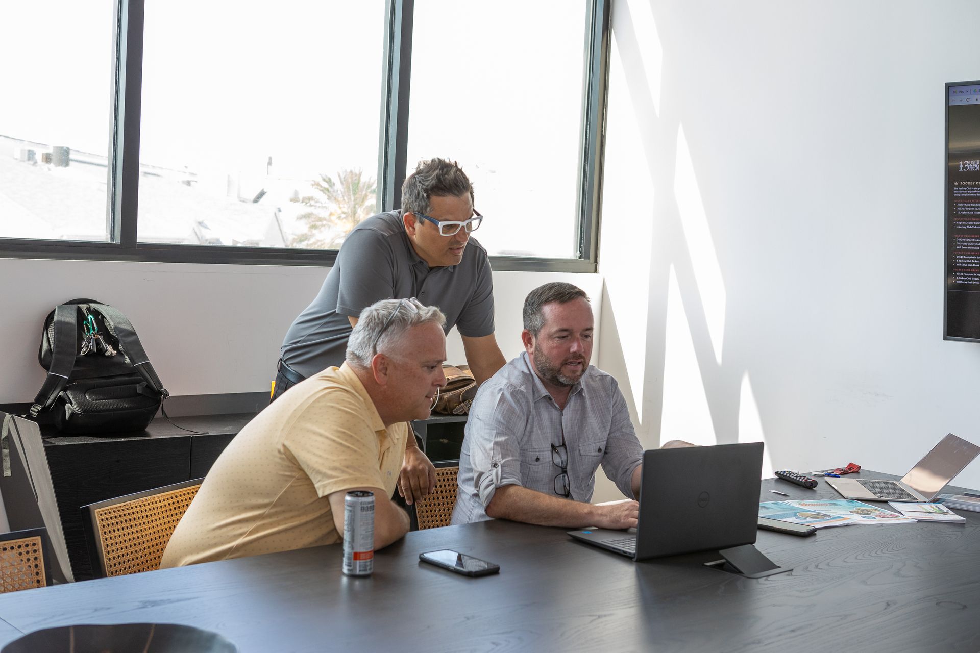 three men are sitting at a table looking at a laptop computer .