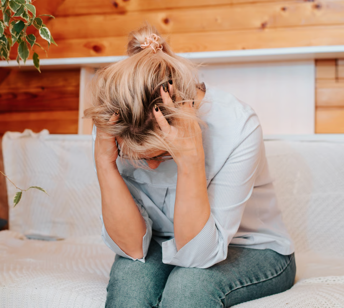 Woman sitting on a couch with head in hands, looking down; appears distressed.