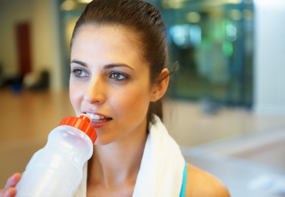a woman is drinking water from a bottle in a gym .