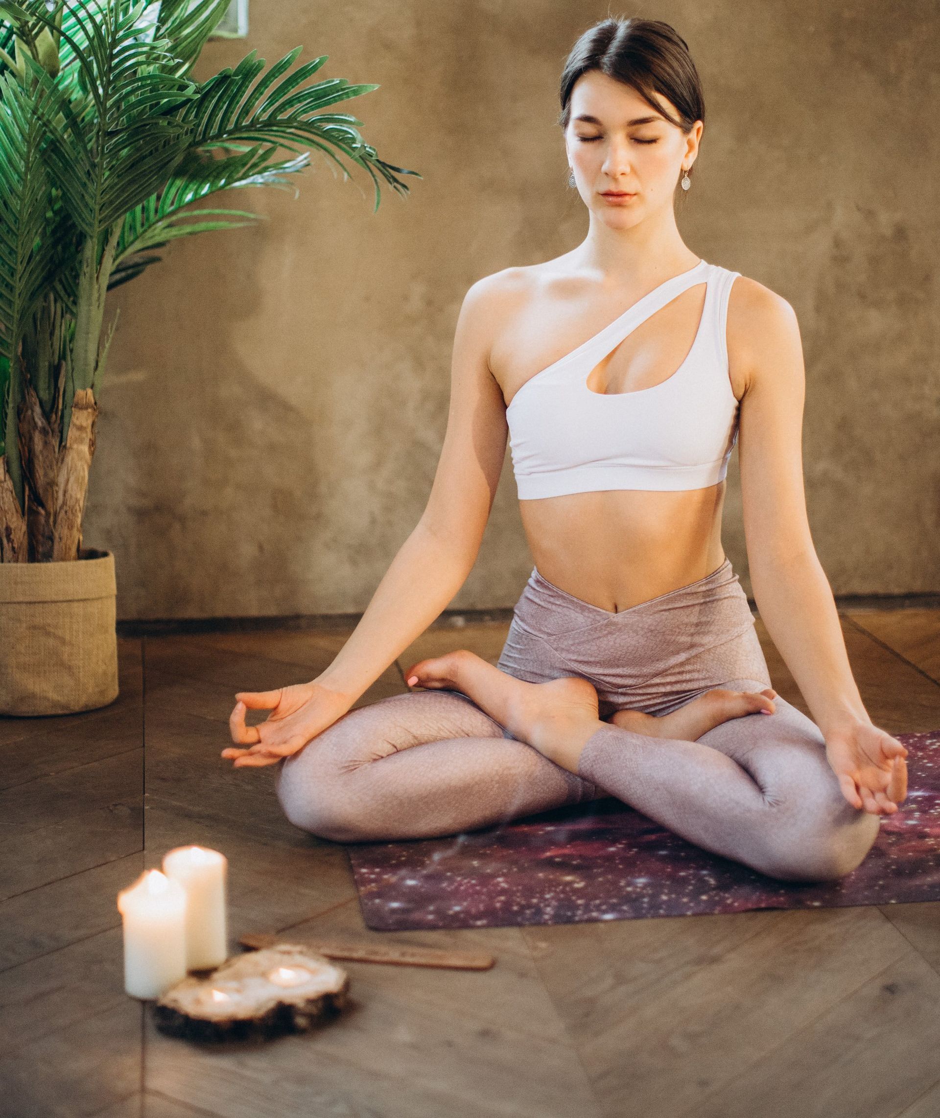 A woman is sitting in a lotus position on a yoga mat next to candles.