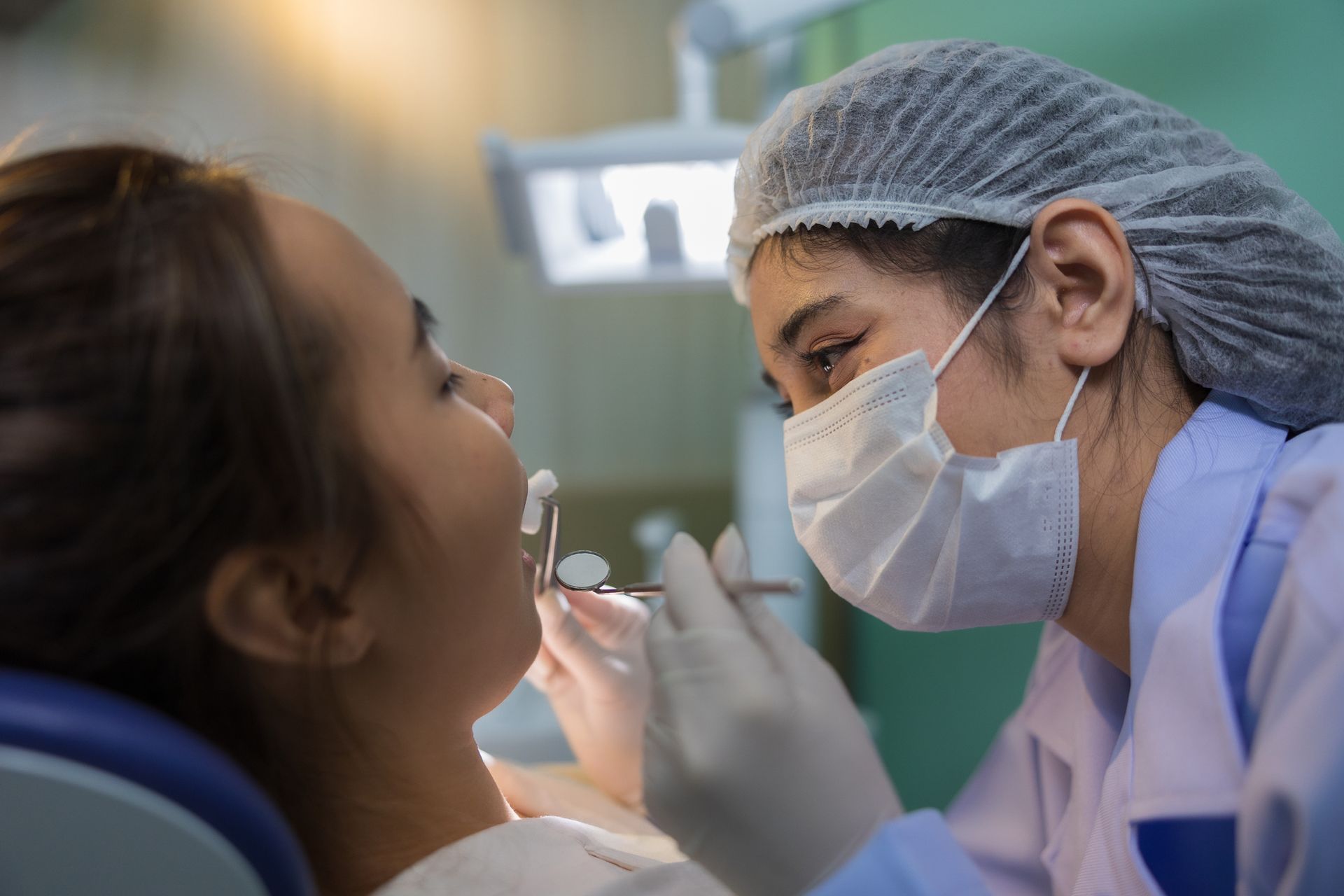 Female dentist checks female patient’s mouth in a dental treatment room.
