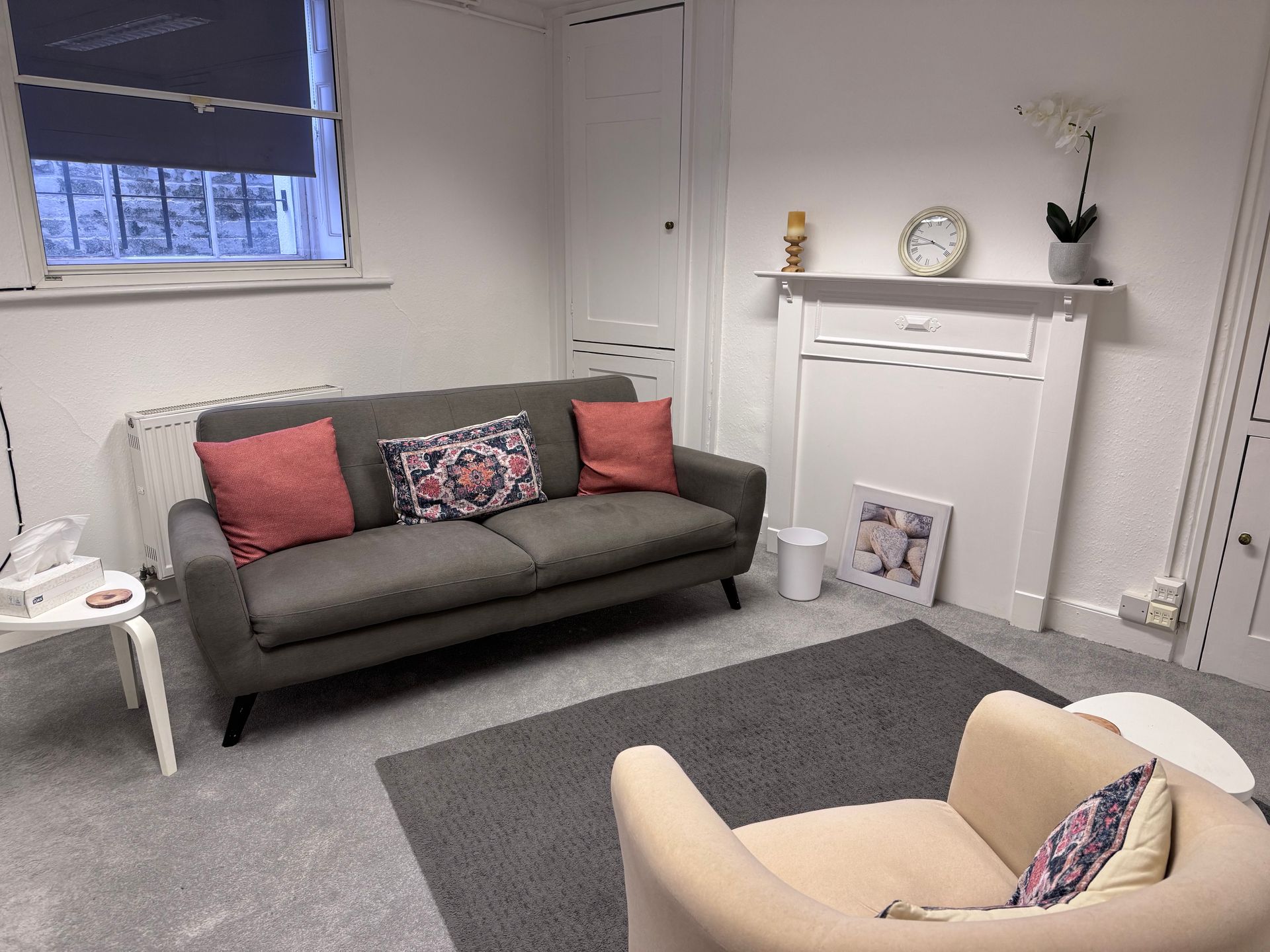 Small living room with gray sofa, pink cushions, cream armchair, fireplace, and gray rug.