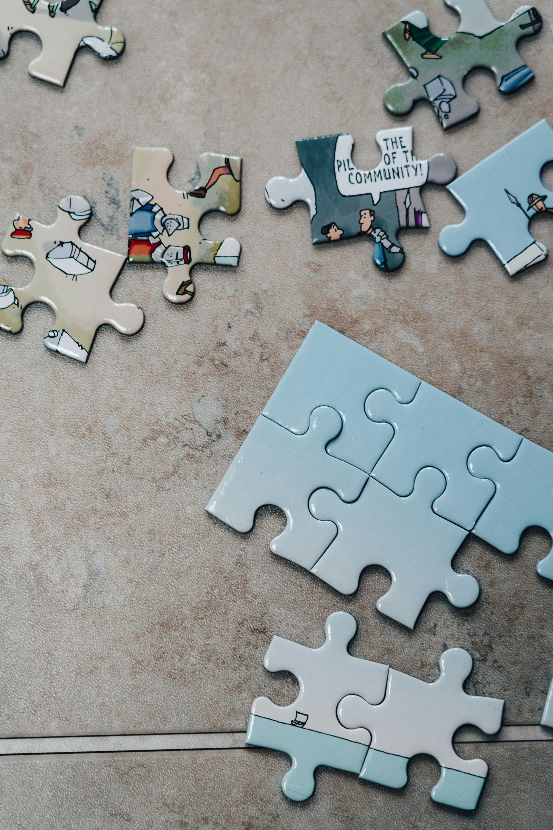 Scattered puzzle pieces on a tabletop, with one partly assembled light blue puzzle in the foreground