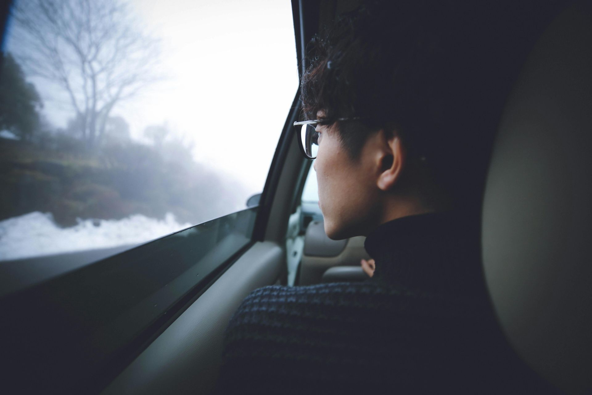 Person in a car looking out foggy window at a road and trees.