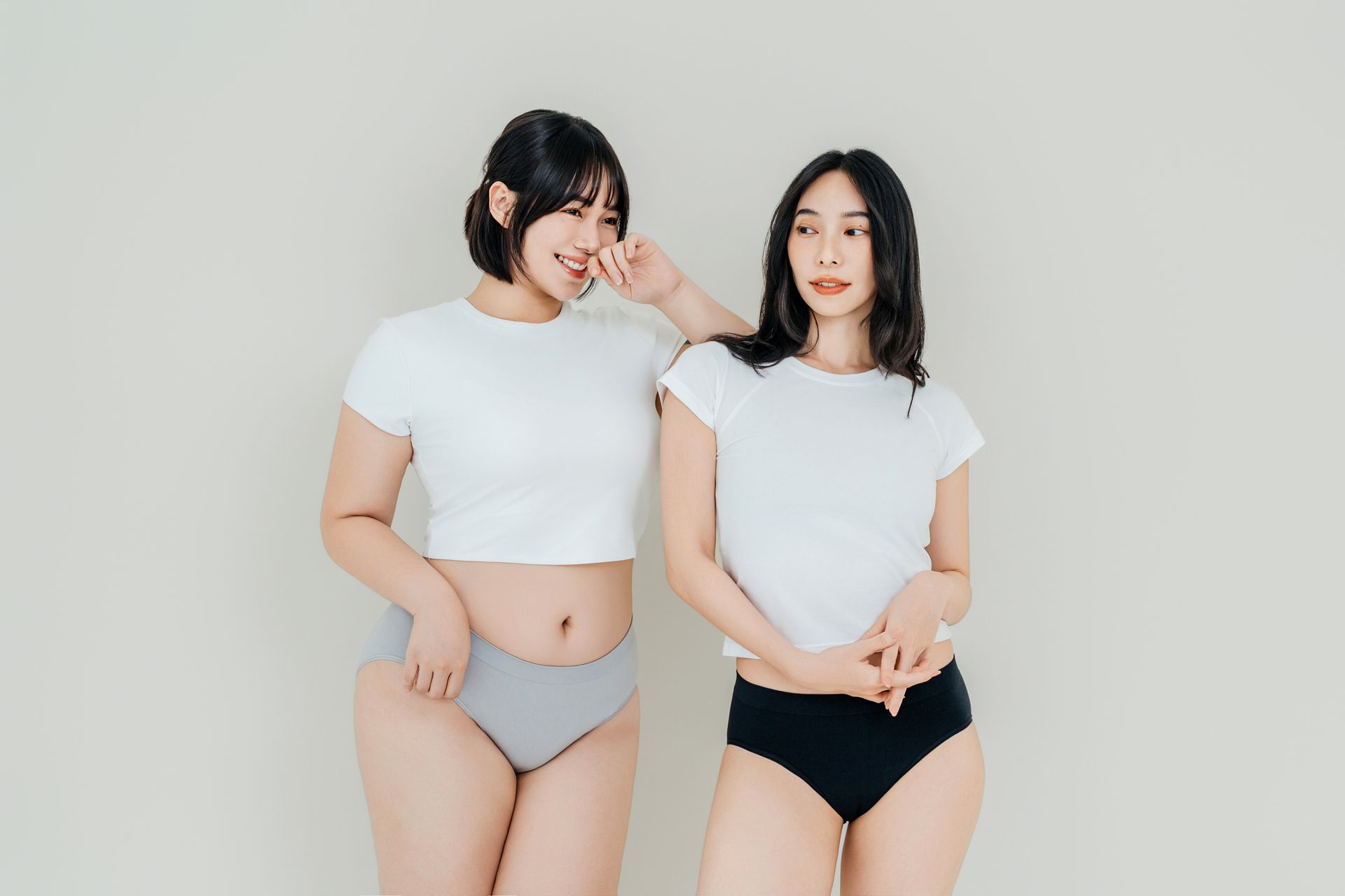 兩名穿著白色上衣和內衣的人在純色淺色背景前擺姿勢。
