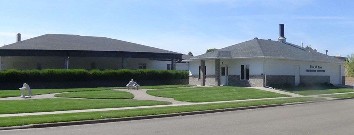 A white building with a dark roof sits in front of green grass and a blue sky.