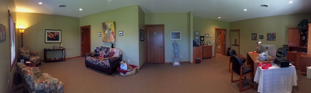 Spacious room with couches, a table, and a desk. Light walls and brown carpet.