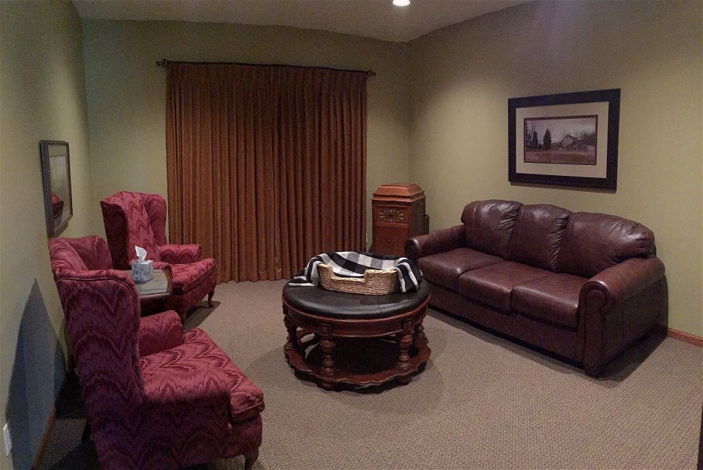 A waiting room with red chairs, brown couch, round table, and framed art.