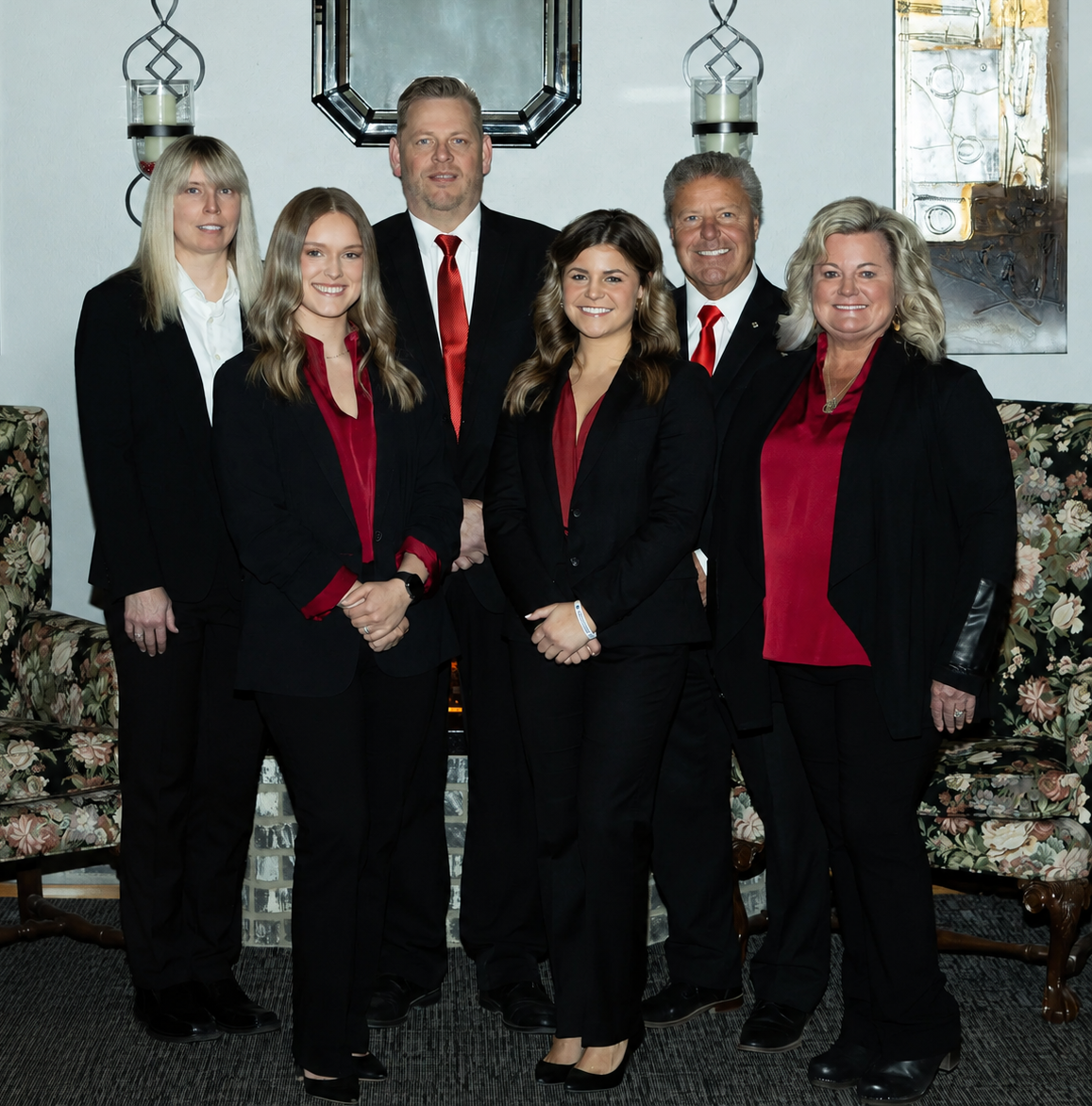 Three people standing in front of a fireplace; two women and a man in formal attire, smiles.