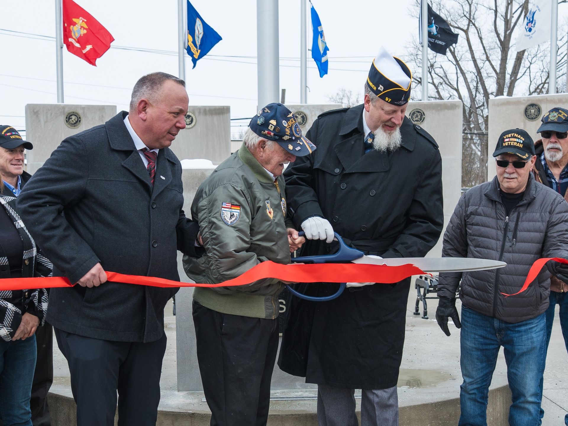 People cutting a red ribbon at a ceremonial event in front of a monument and flags.