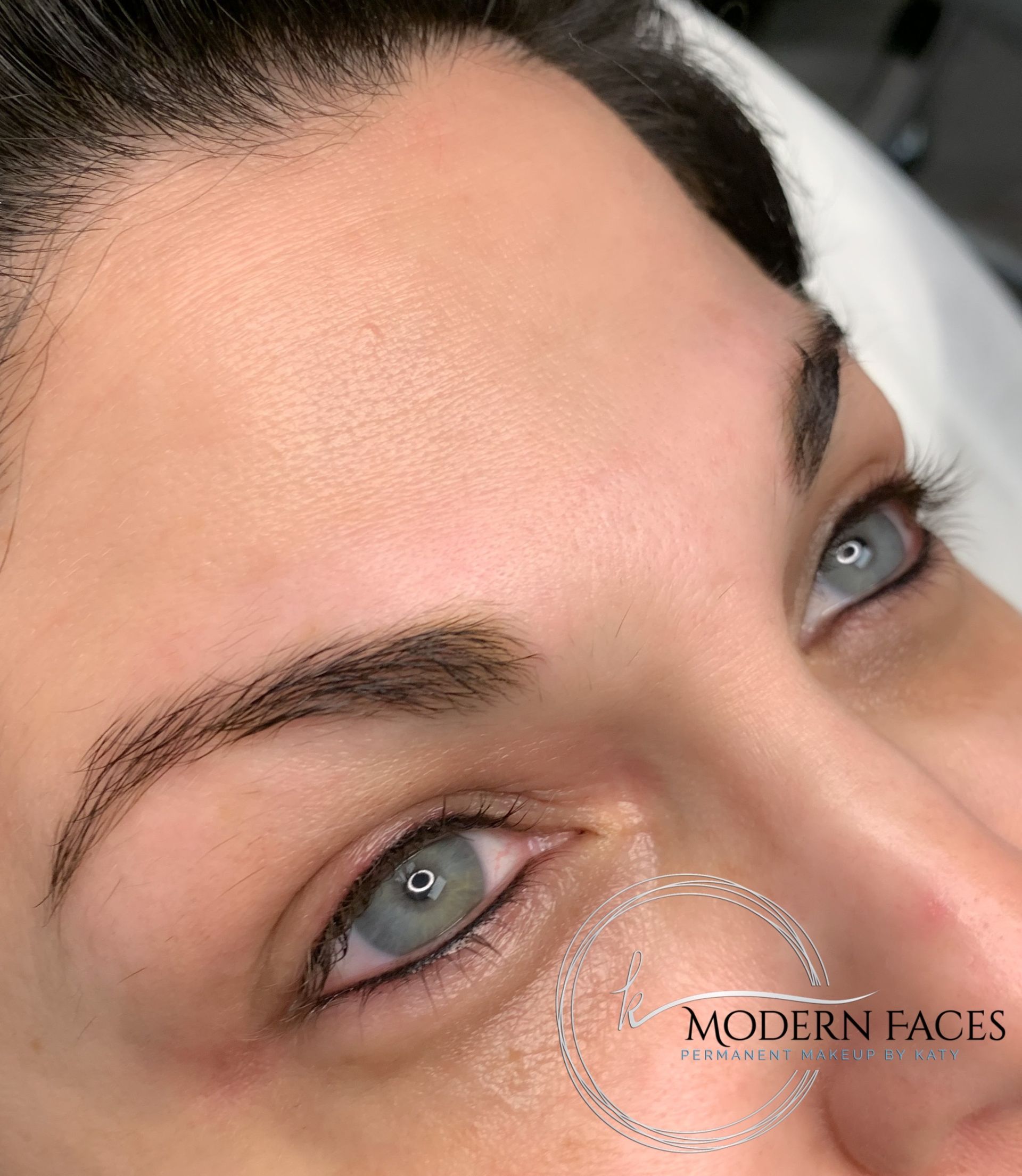 Close-up of a person’s blue eyes and eyebrows with a subtle beauty treatment on the under-eye area
