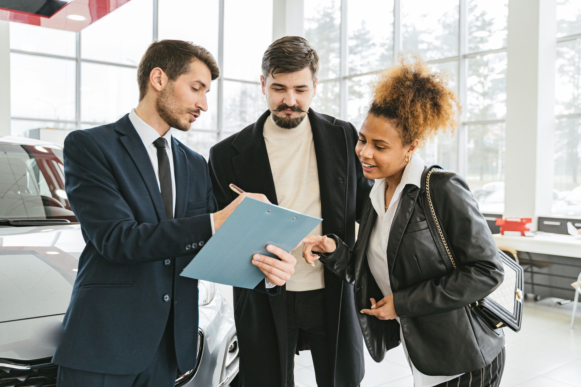 Car salesperson shows document to a couple in a car showroom.