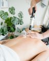 A person receiving a back cupping treatment in a bright spa room, with a handheld massage device applied to the skin.