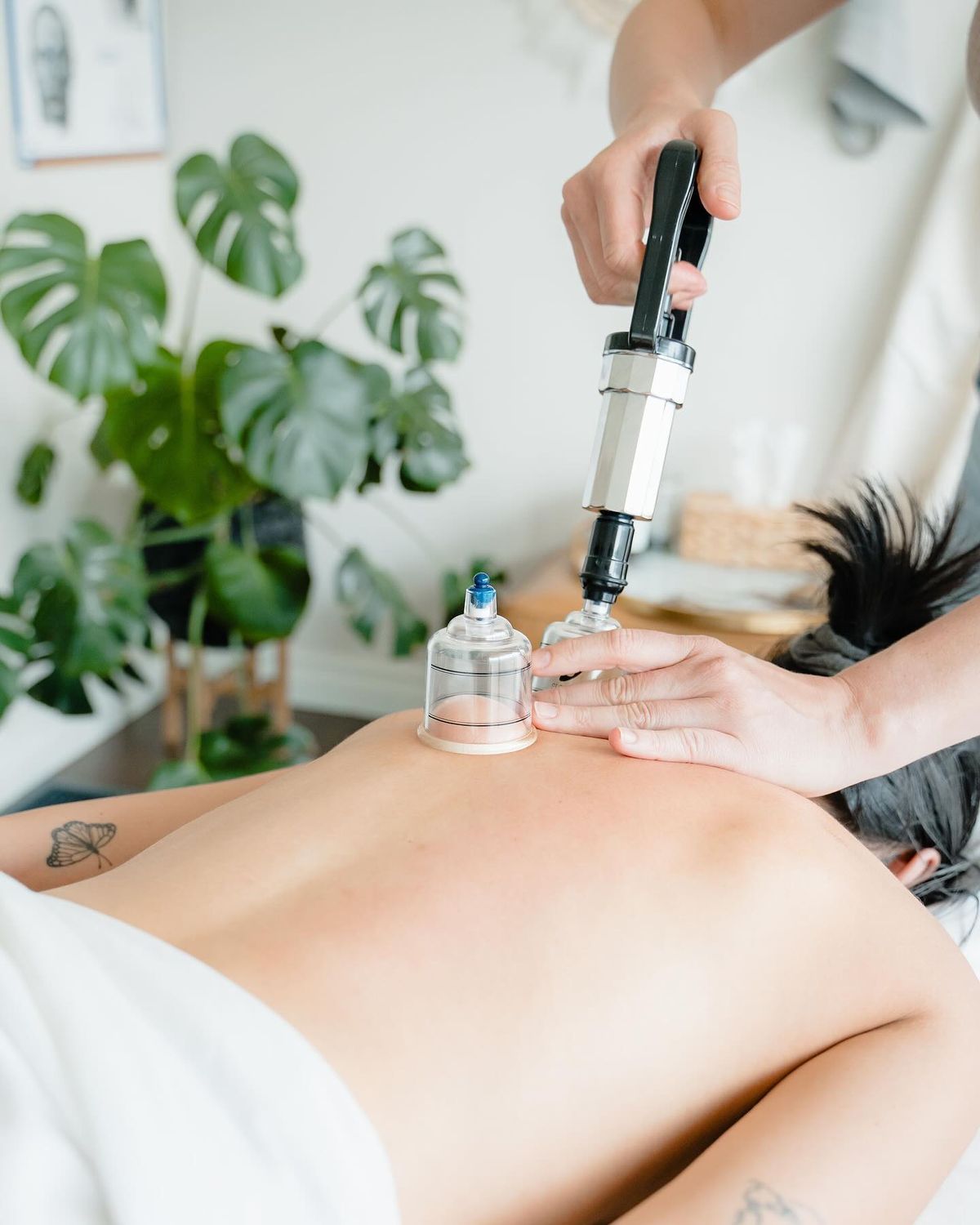 A person receiving a back cupping treatment in a bright spa room, with a handheld massage device applied to the skin.