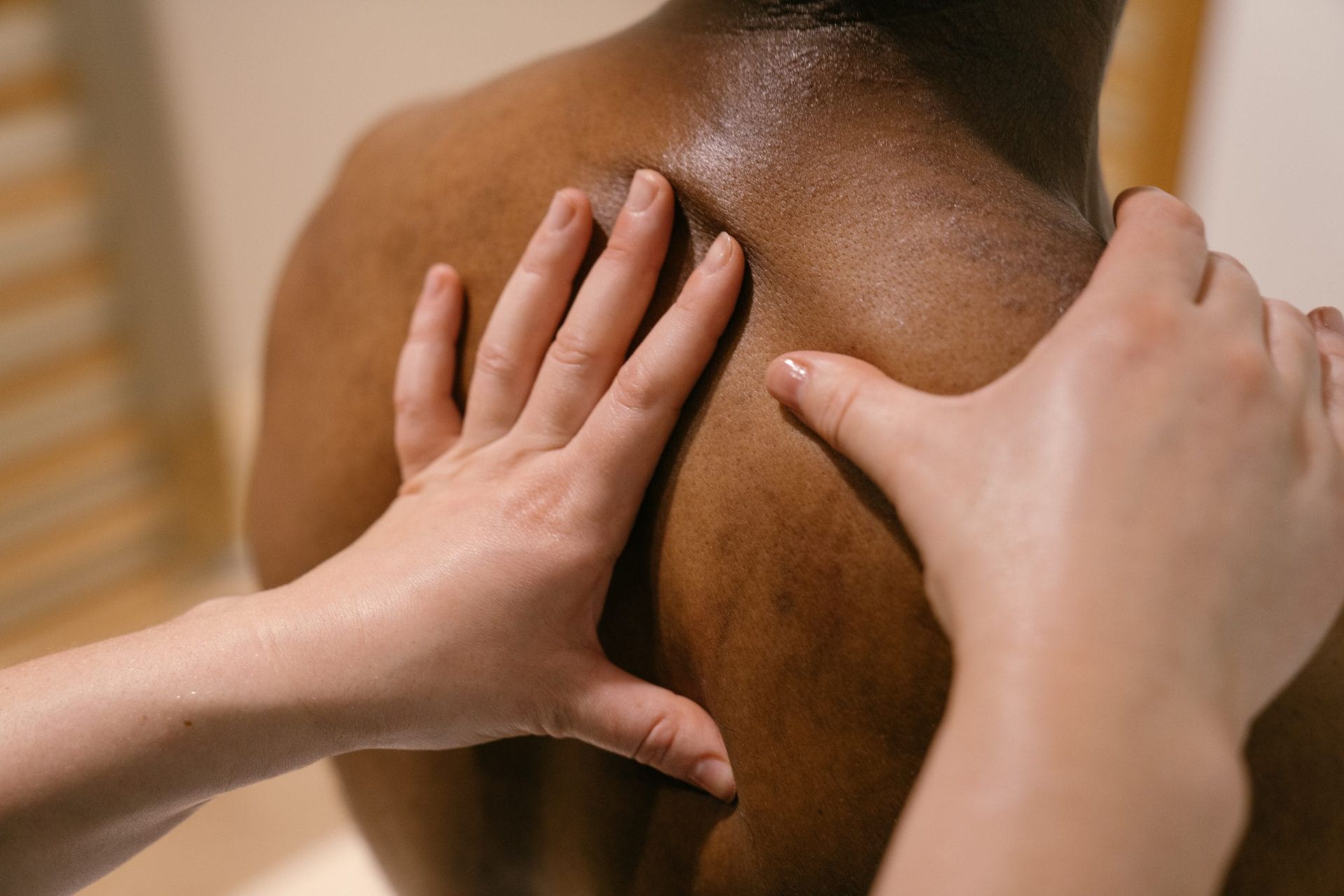 Hands massaging a person’s upper back and shoulder skin in a close-up view.