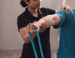 Physical therapist guiding arm stretches with teal resistance band in a clinic setting