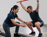Trainer assists a man doing a squat with a barbell in a gym