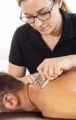 Therapist using a massage tool on a client’s back in a bright treatment room