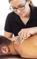 Therapist using a massage tool on a client’s back in a bright treatment room