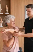Physical therapist guiding a client through an arm stretch in a bright clinic room