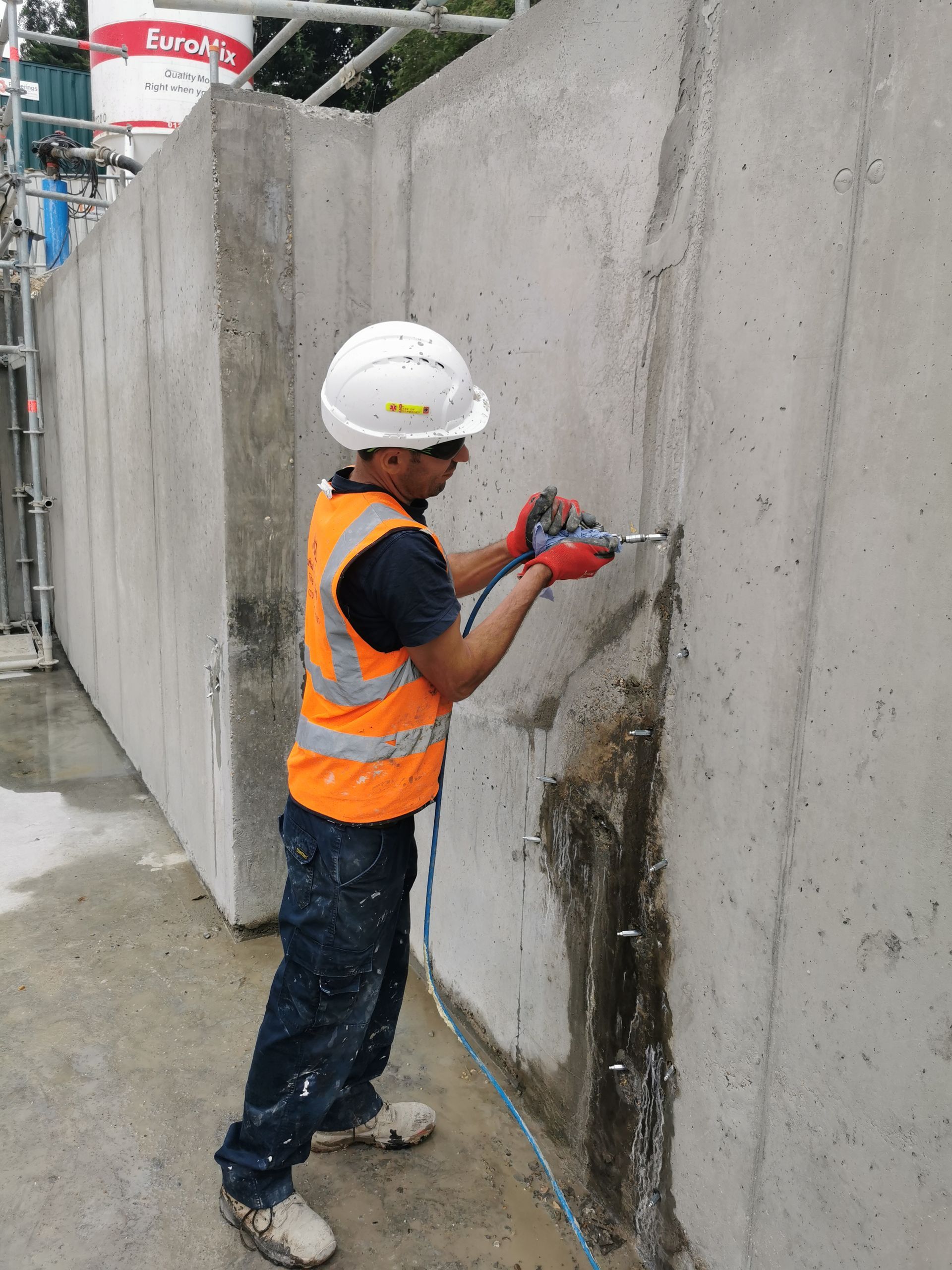 A construction worker is using a drill on a concrete wall.